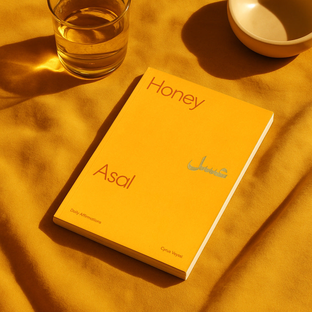 Yellow book titled 'Honey Asal' on a yellow surface with a glass of water and bowl.